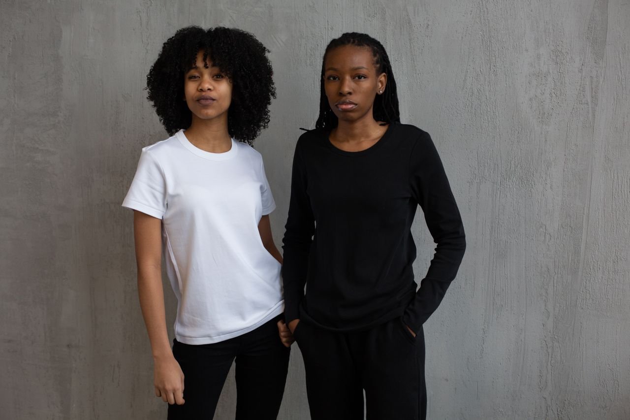 African American female model in black sports suit standing with hand in pocket near curly haired woman in t shirt